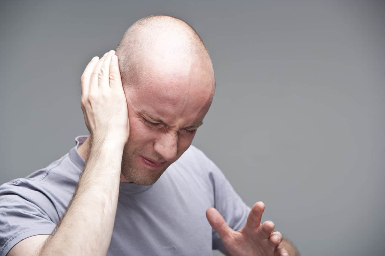 Photo of a man holding one ear and wincing in pain