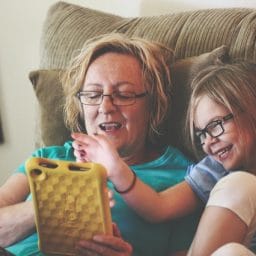 Woman and girl sit in a recliner while playing with a tablet