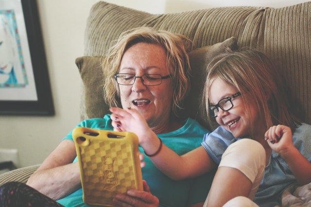 Woman and girl sit in a recliner while playing with a tablet