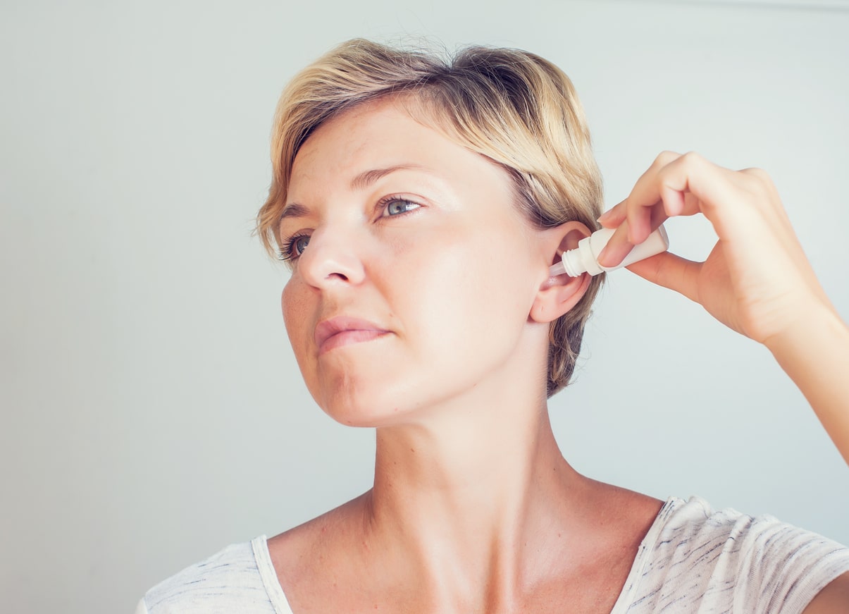 Woman using ear drops in front of gray background