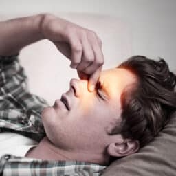 Man on couch suffering from sinus infection pinching nose