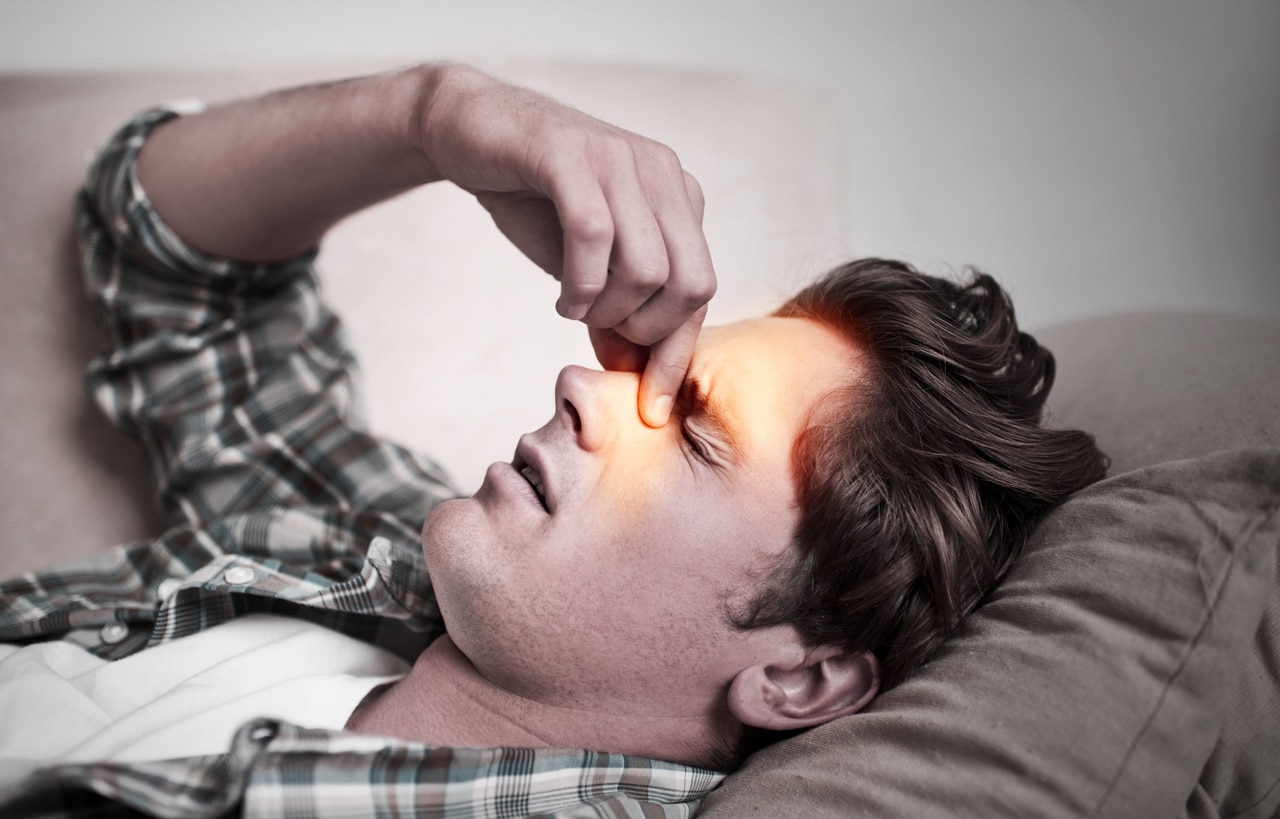 Man on couch suffering from sinus infection pinching nose